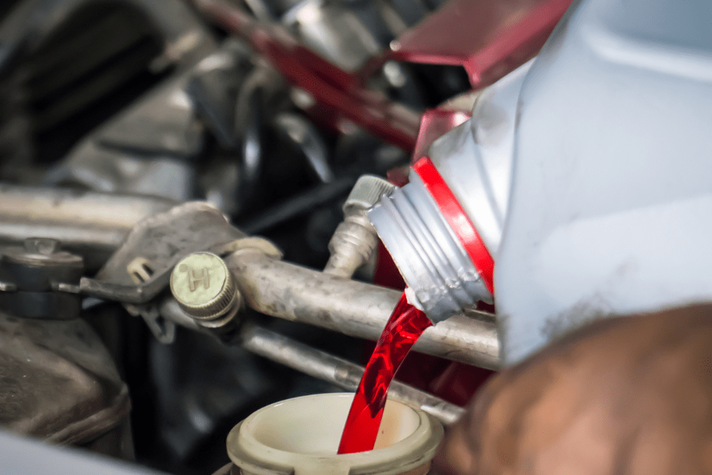 The Importance of Regular Fluid Top-Offs for Your Vehicle’s Longevity. in Marion, Il. Image of red coolant being poured into the coolant reservoir on a car that came. in for fluid exchanges.