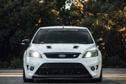 top car brands, auto repair in Marion IL at Hale's Automotive. Front view of a white Ford Focus ST with headlights on, parked outdoors.